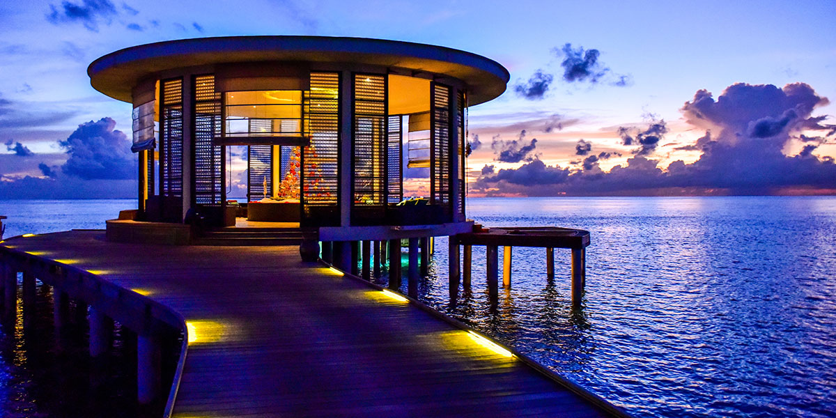 photo of a cottage on the ocean in maldives with evening light, clouds and calm waters
