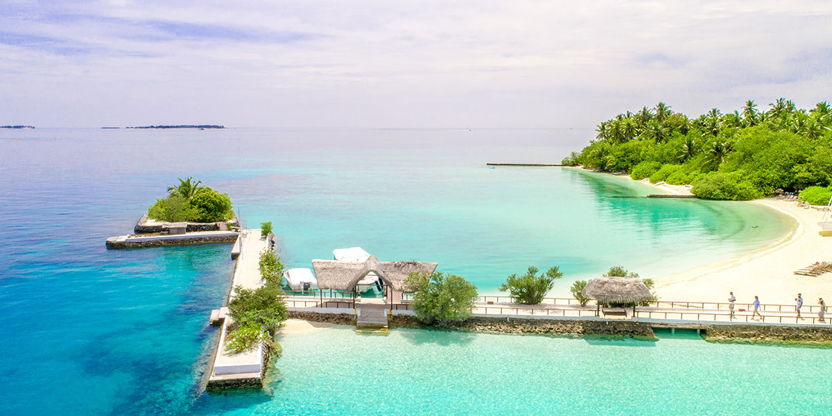 a resort in Maldives with people walking on a ramp towards cottages
