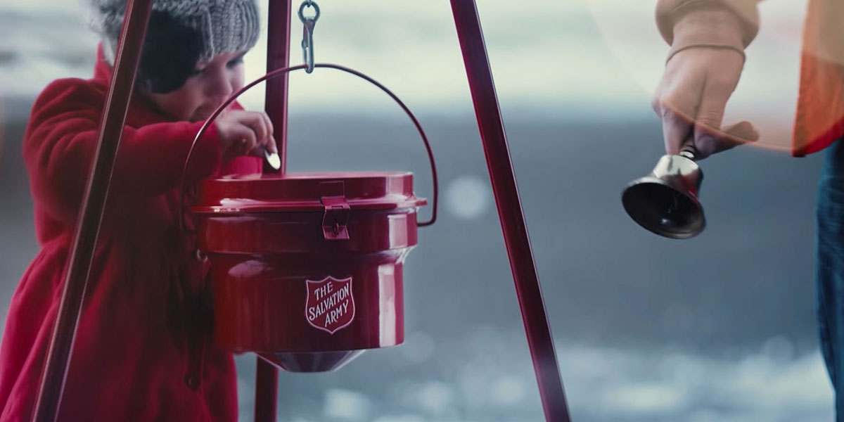 a salvation army charity tin and a child putting a coin in while a man with a charity bell rings